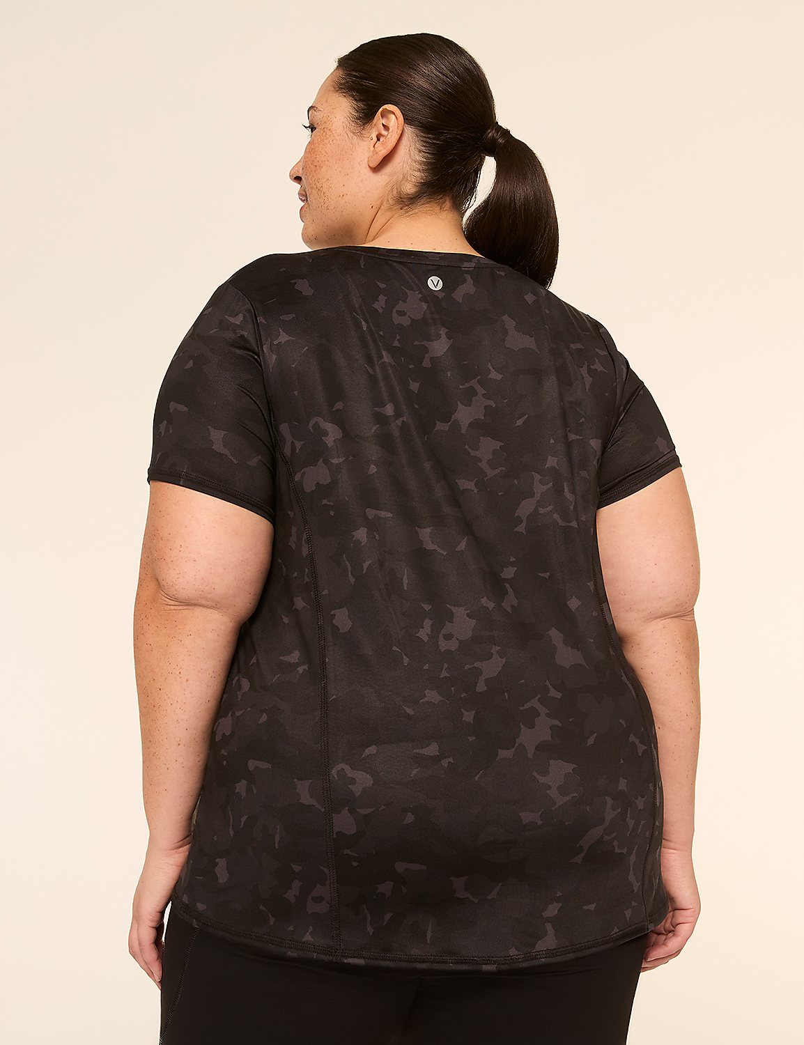 A woman in a black camouflage t-shirt stands against a plain, light-colored background. Product Image 2