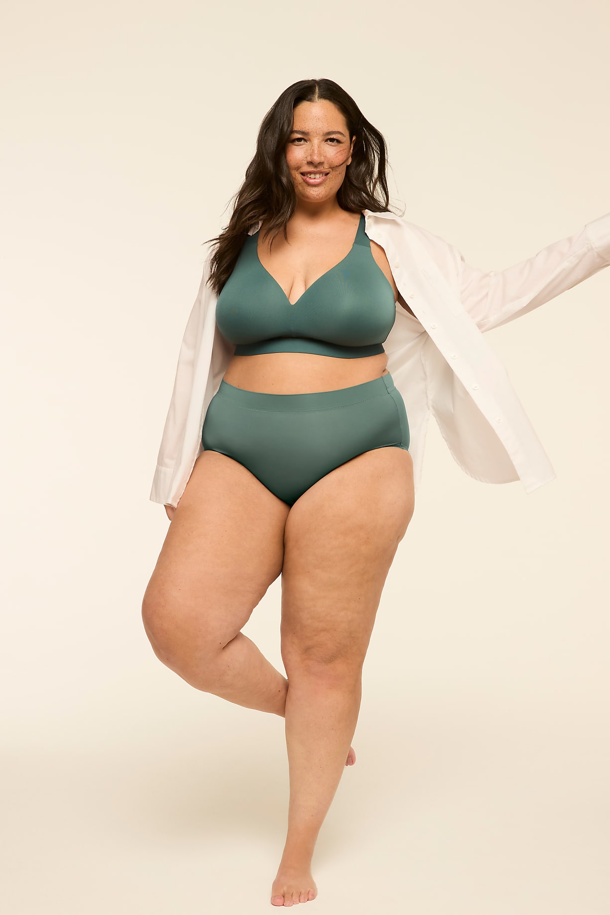 A smiling woman in teal lingerie and an open white shirt stands on one leg against a plain, light background. Product Image 7