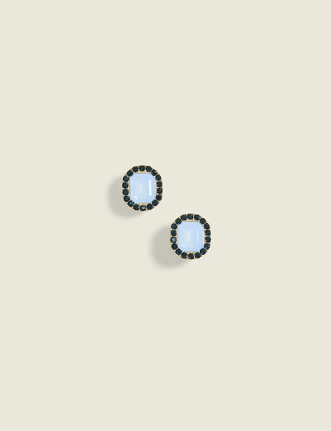 Two oval earrings with light blue stones and black gem borders rest on a plain, light beige background. Product Image 1