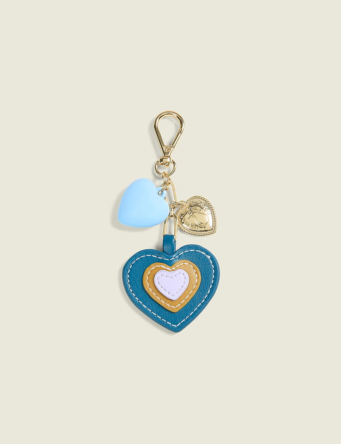 A teal, heart-shaped keychain with layered hearts and small charms hangs against a pale yellow background. Product Image 1