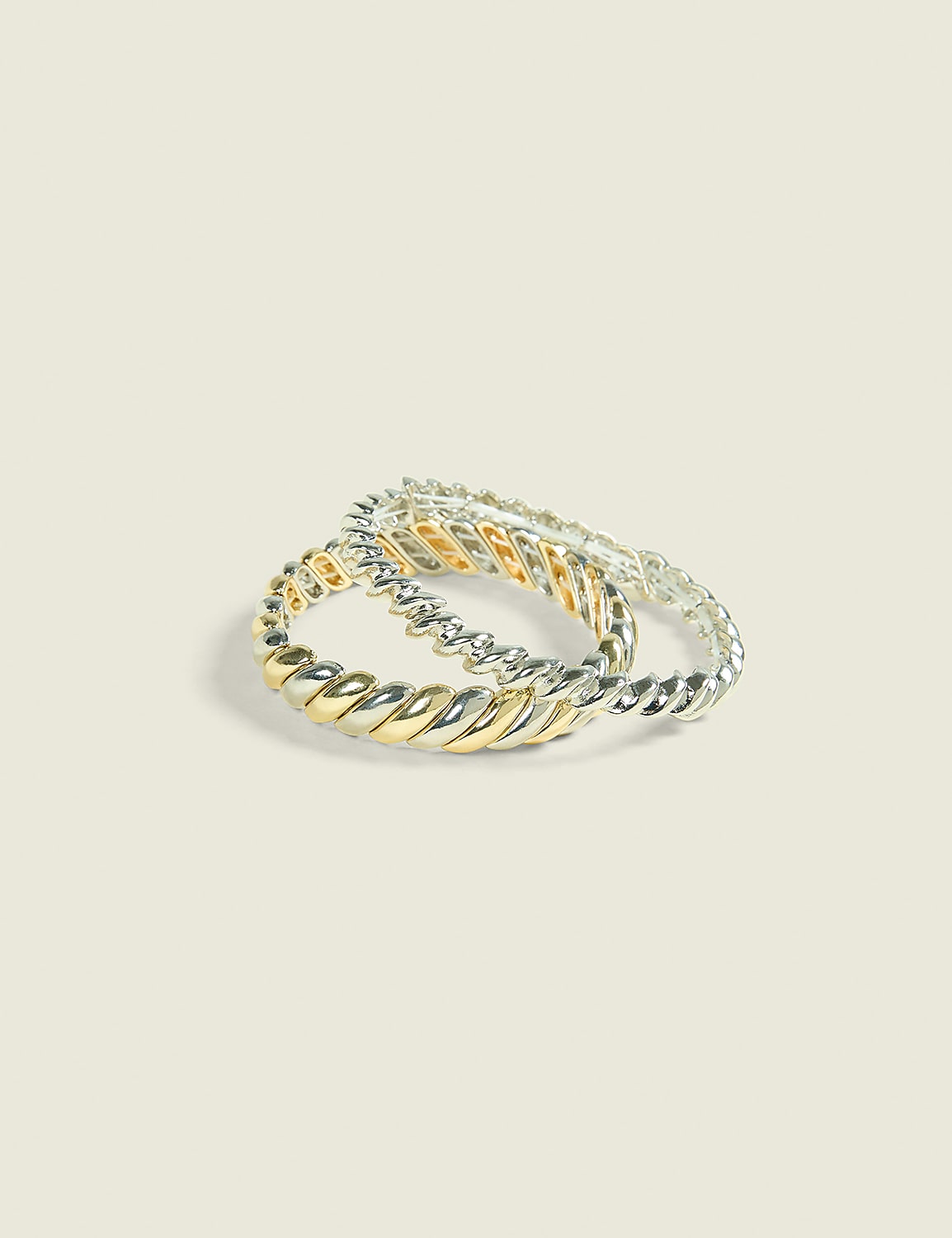 Two twisted rings, one with gold and silver sections and the other entirely silver, rest on a plain, light-colored background. Product Image 1