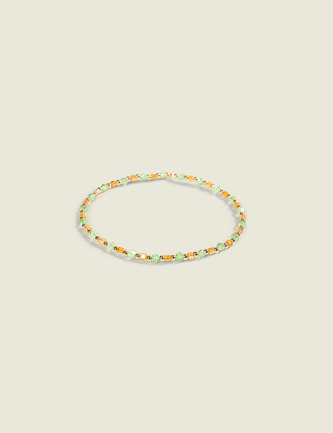 A delicate bracelet with small green and orange beads rests on a plain, light-colored background. Product Image 1