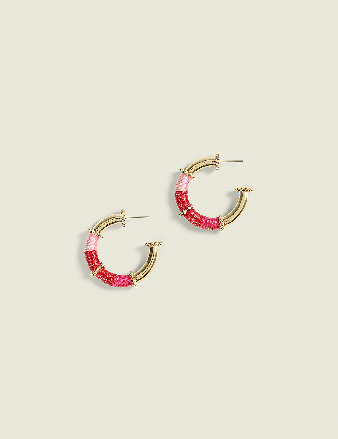 A pair of gold hoop earrings wrapped in pink and red thread rest on a pale green background. Product Image 1
