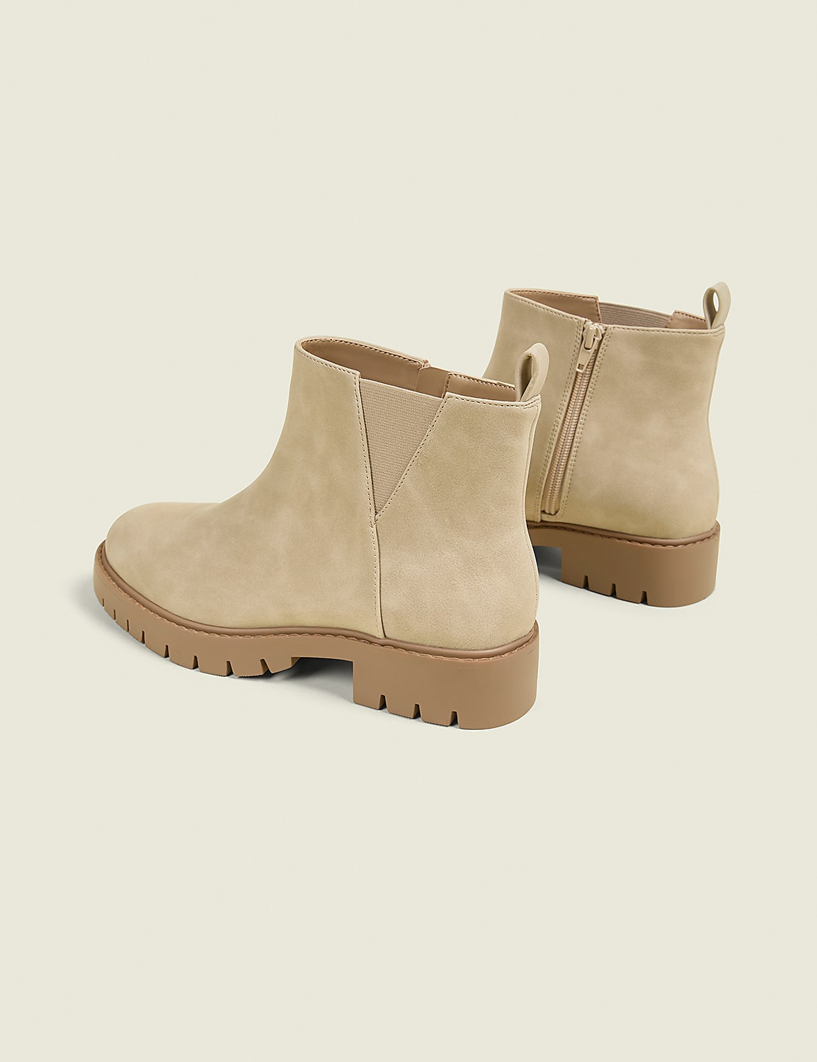 A pair of tan suede ankle boots with thick lug soles are displayed against a plain, light beige background. Product Image 2