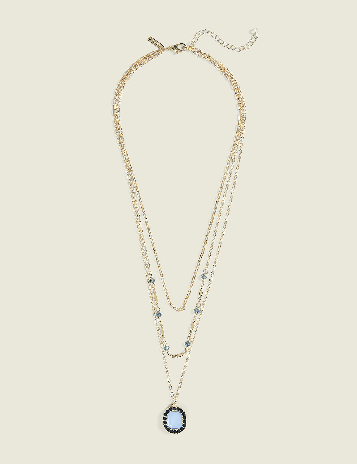 A layered gold necklace with a blue pendant rests against a plain, light beige background. Product Image 1