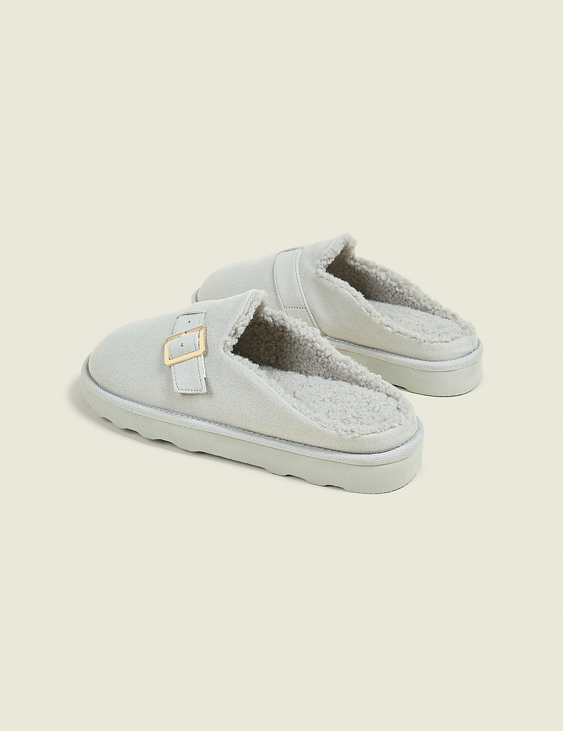 A pair of light gray, fuzzy-lined clogs with gold buckles rest on a pale gray background. Product Image 2