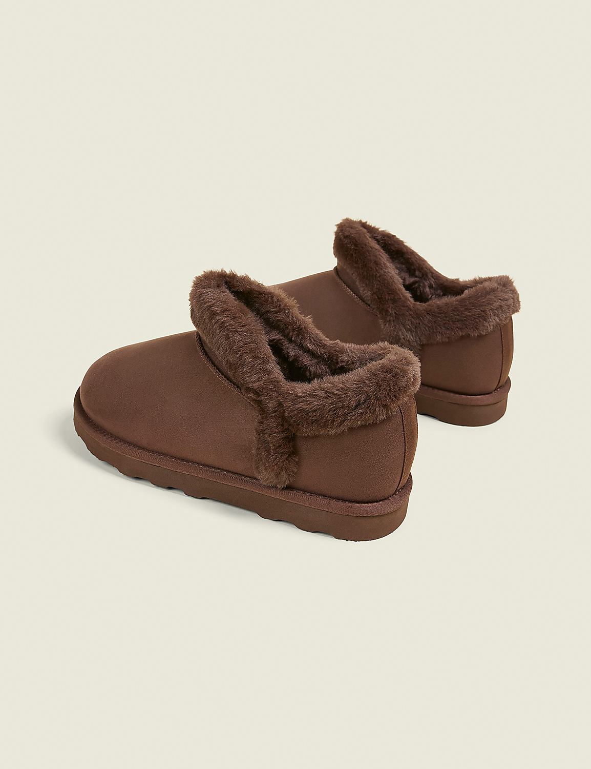A pair of brown, fuzzy-lined slippers rests on a plain, light brown background. Product Image 2