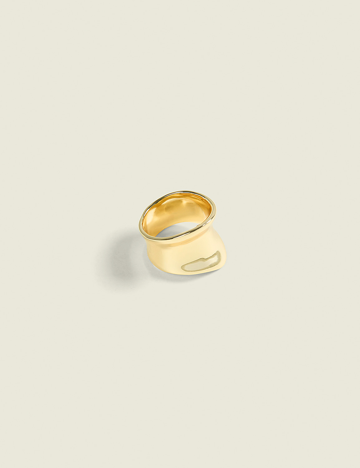 A gold ring with an organic, flowing design rests on a soft, light-colored surface, casting a subtle shadow. Product Image 1