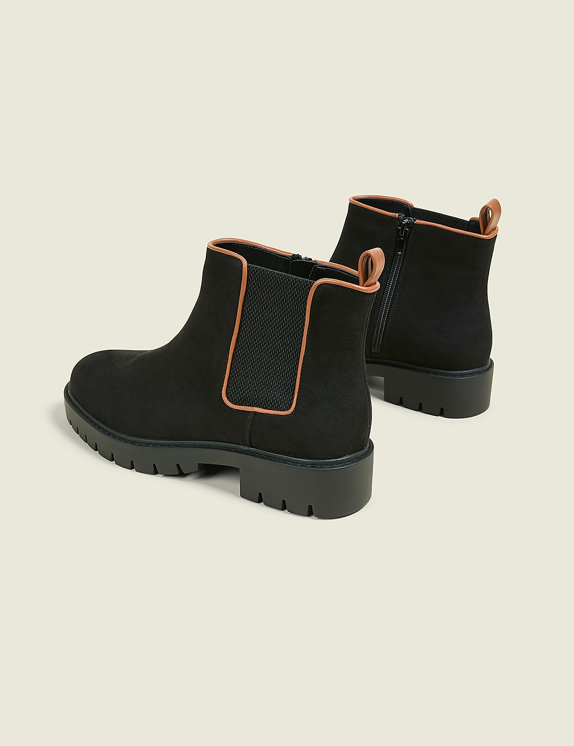 A pair of black Chelsea boots with tan trim and lug soles rests on a plain, light-colored background. Product Image 2