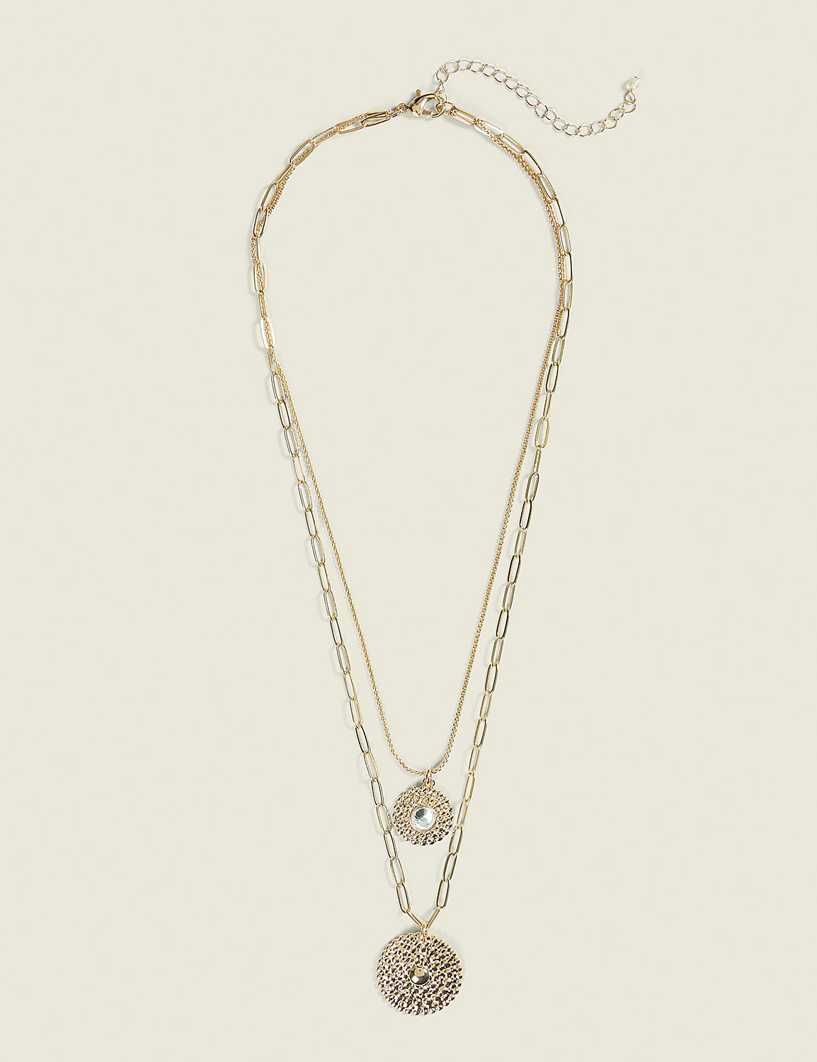 A layered gold necklace with two circular pendants hangs against a plain, light beige background. Product Image 1
