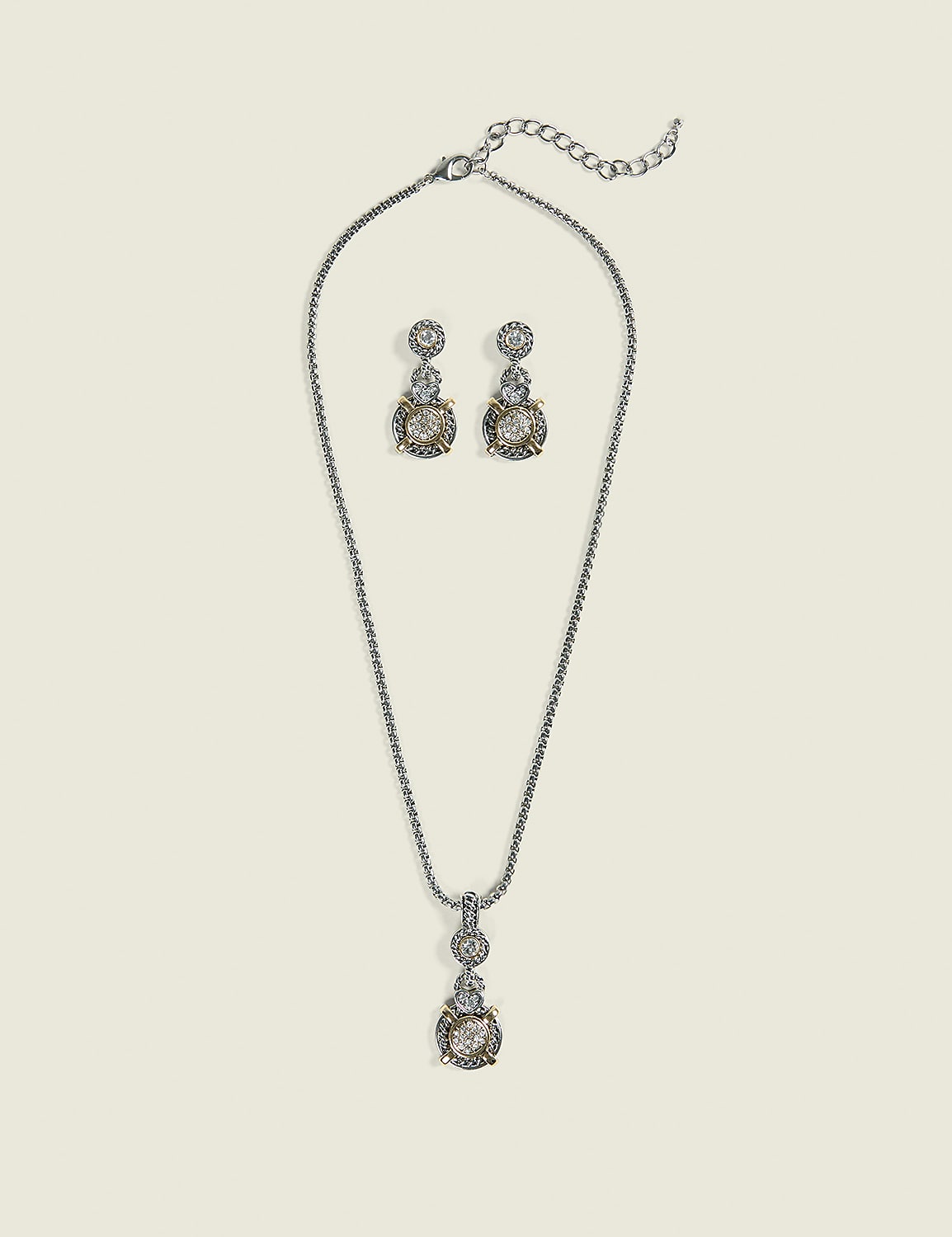 A silver necklace with a pendant and matching earrings, adorned with clear stones and gold accents, are displayed against a pale, textured background. Product Image 1