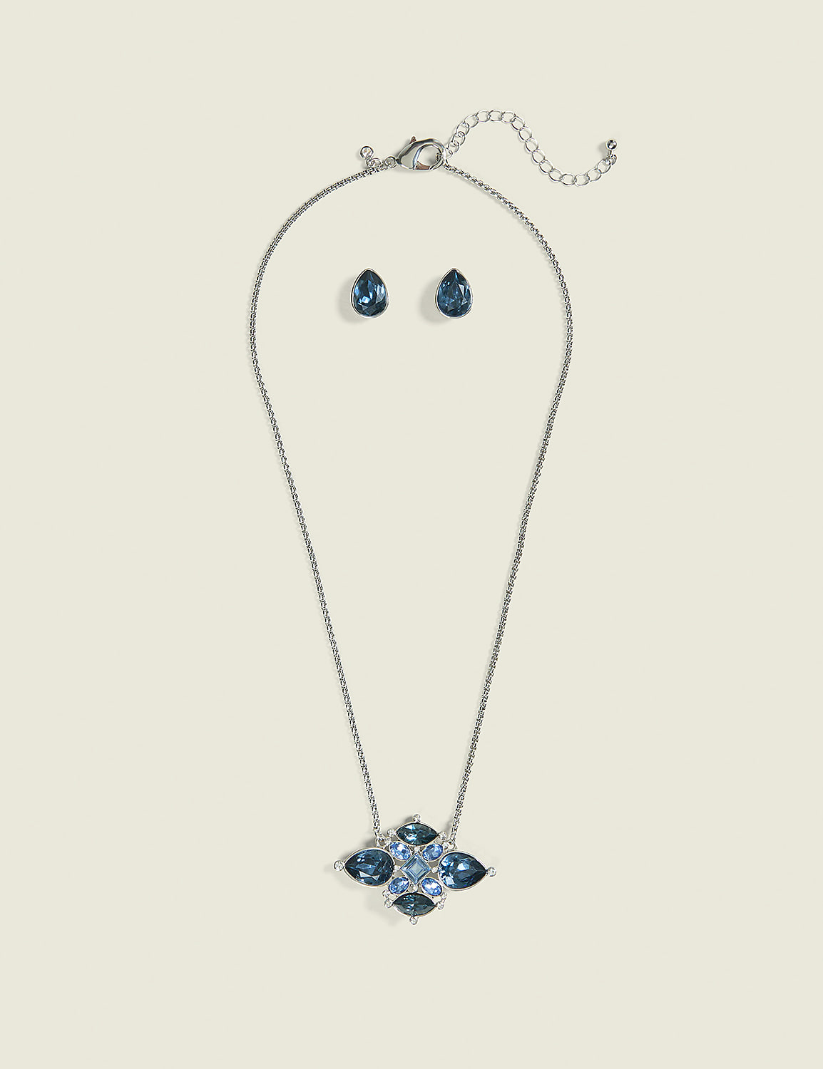 A silver necklace with a blue jeweled pendant and matching teardrop earrings are displayed against a plain, light-colored background. Product Image 1