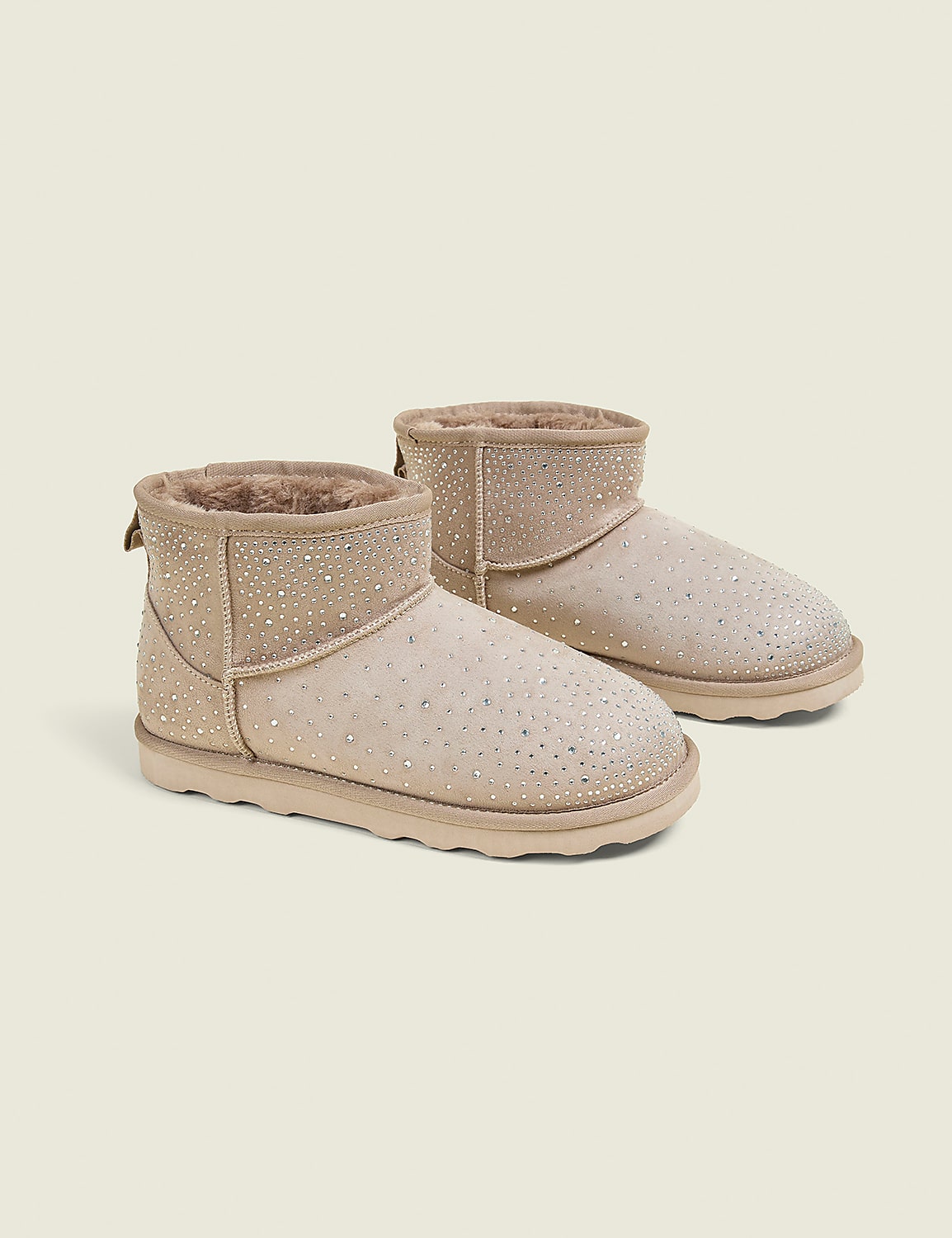 A pair of beige, rhinestone-embellished ankle boots with fluffy lining are displayed against a plain, light beige background. Product Image 1