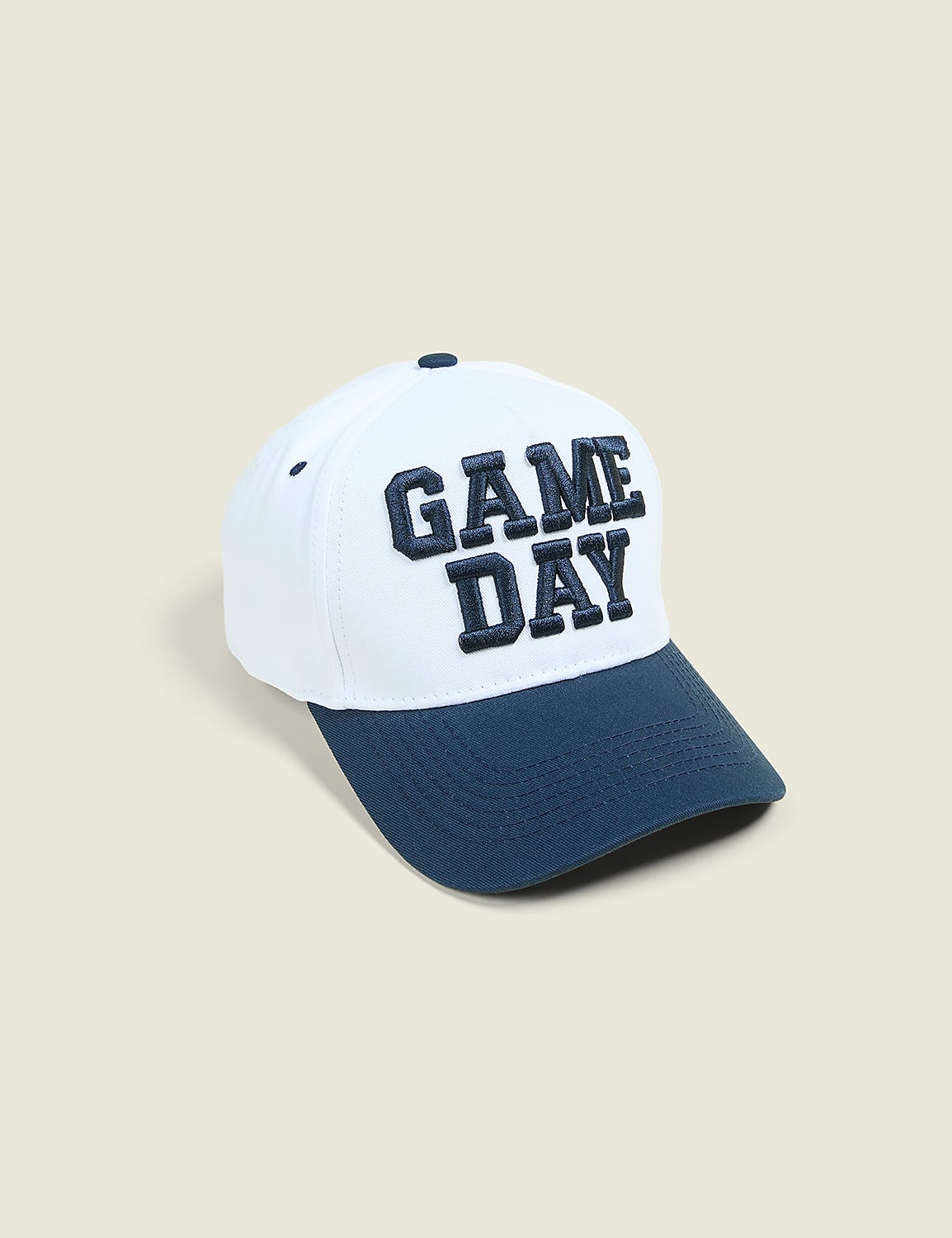 A white baseball cap with "GAME DAY" embroidered in navy blue sits on a plain, light beige background. Product Image 1
