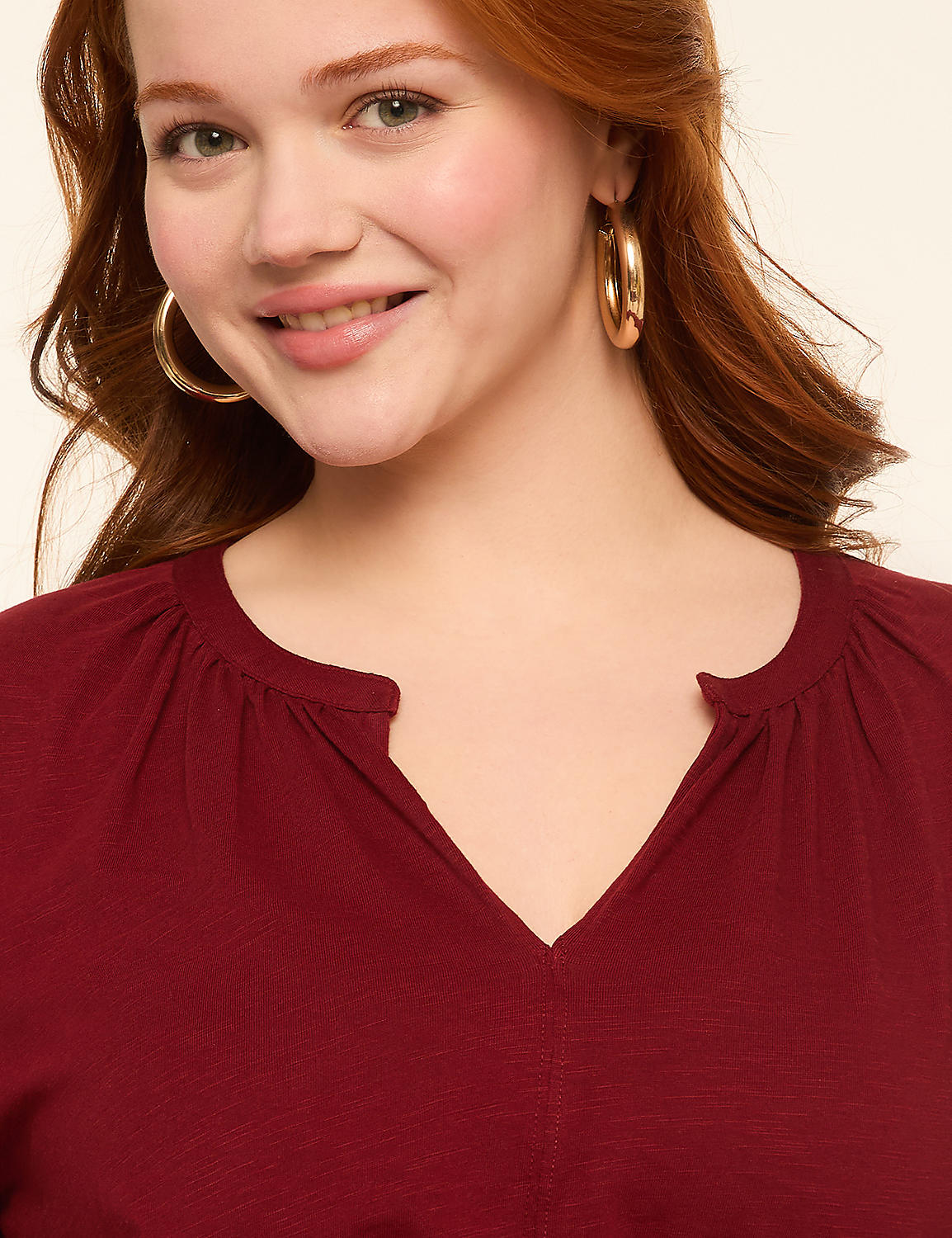 A smiling woman with red hair and large hoop earrings wears a maroon v-neck top against a plain, light background. Product Image 3
