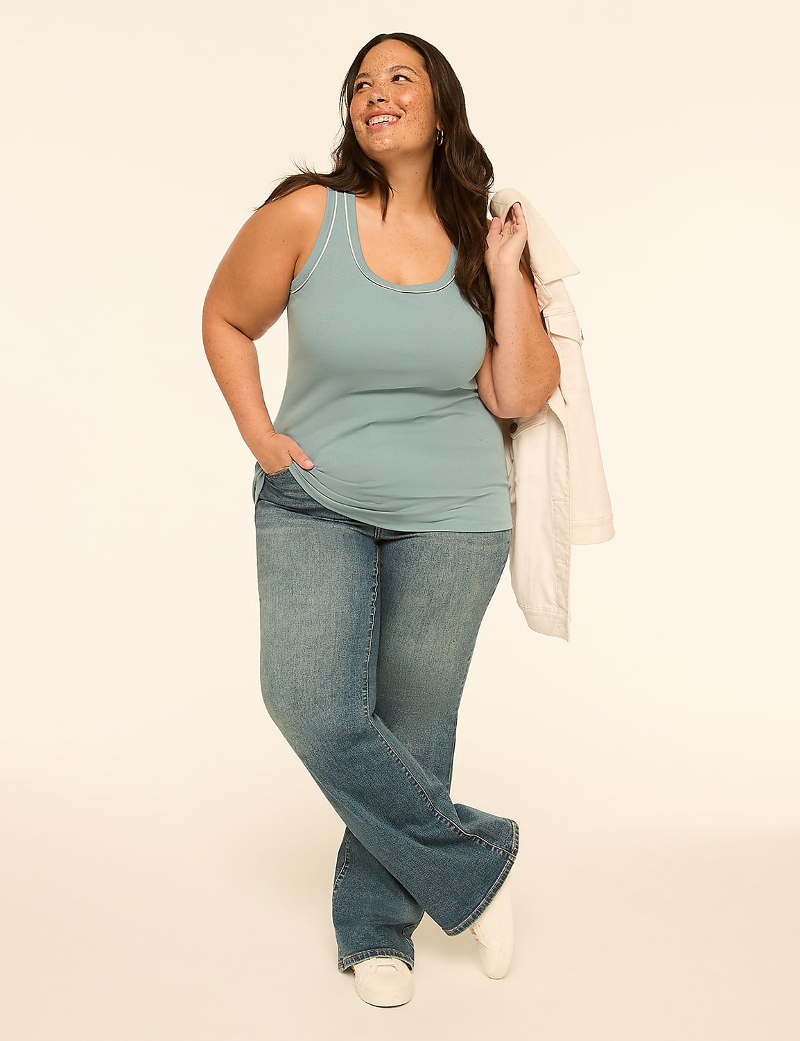 A woman in a blue tank top and jeans stands with a jacket draped over her shoulder against a plain, light-colored background. Product Image 3