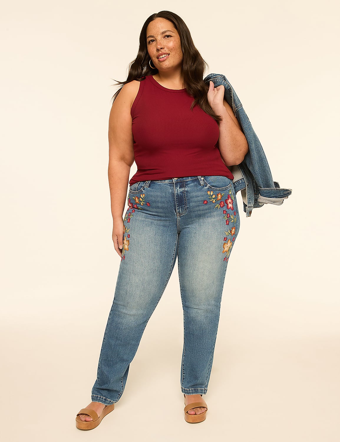 A woman in a maroon tank top and embroidered jeans stands against a plain, light-colored background, holding a denim jacket over her shoulder. Product Image 3