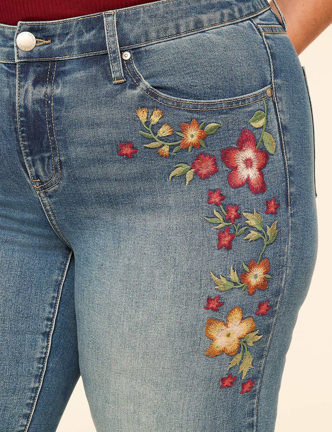 Close-up of blue denim jeans with colorful floral embroidery on the right hip, against a plain, light-colored background. Product Image 4