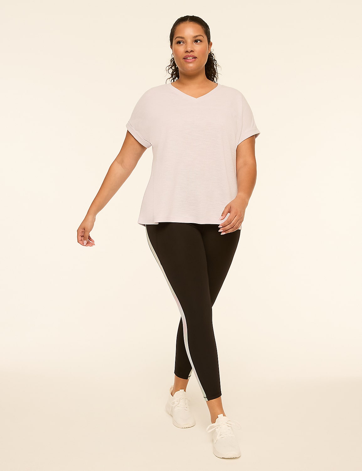 A woman in a light gray t-shirt and black leggings with a white stripe walks forward against a plain, light background. Product Image 3
