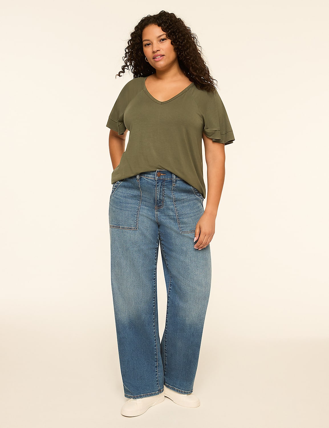 A woman in a green v-neck t-shirt and wide-leg jeans stands against a plain, light-colored background. Product Image 3