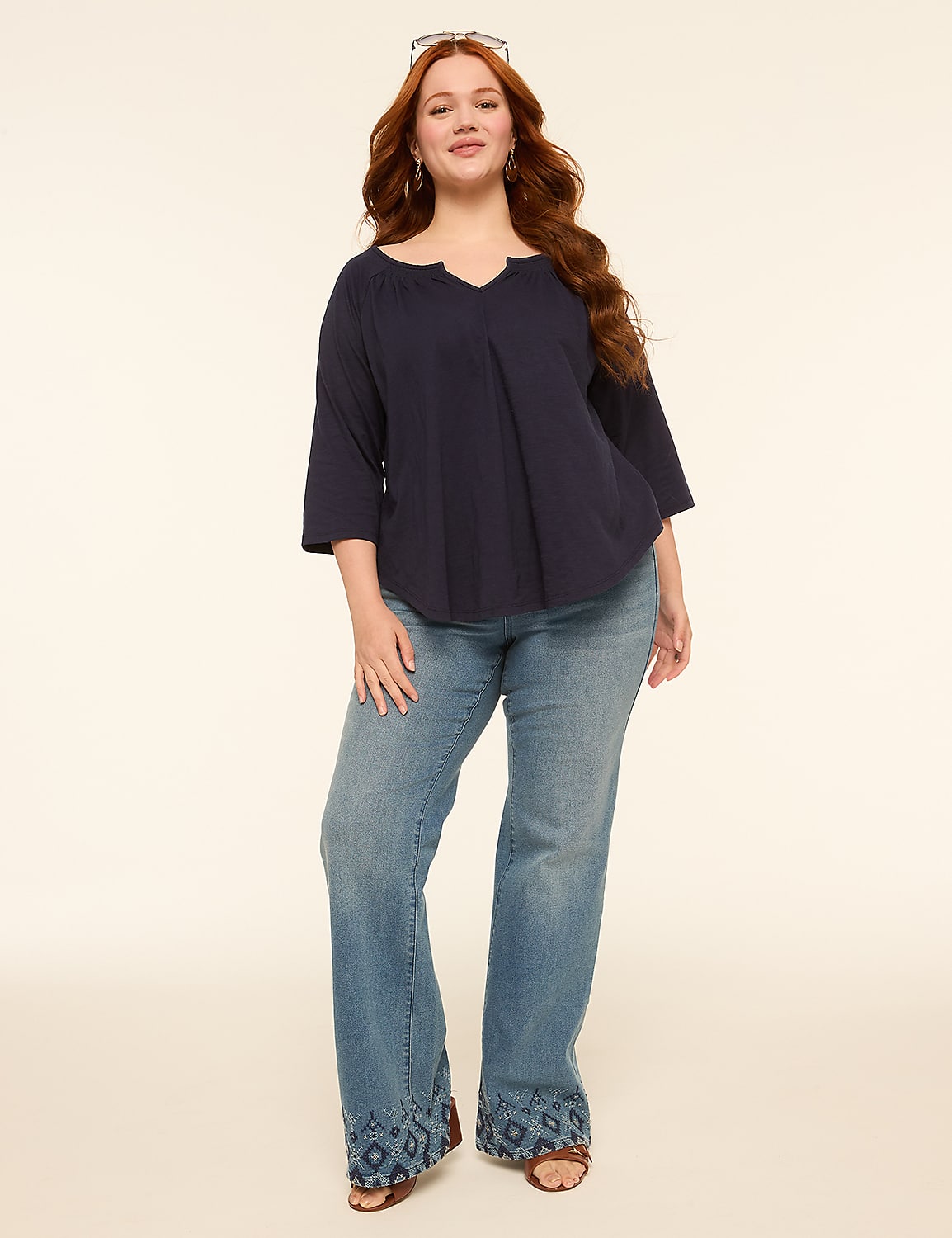 A woman with long red hair stands in the foreground wearing a navy blue top and flared jeans with embroidered hems, against a plain, light-colored background. Product Image 3