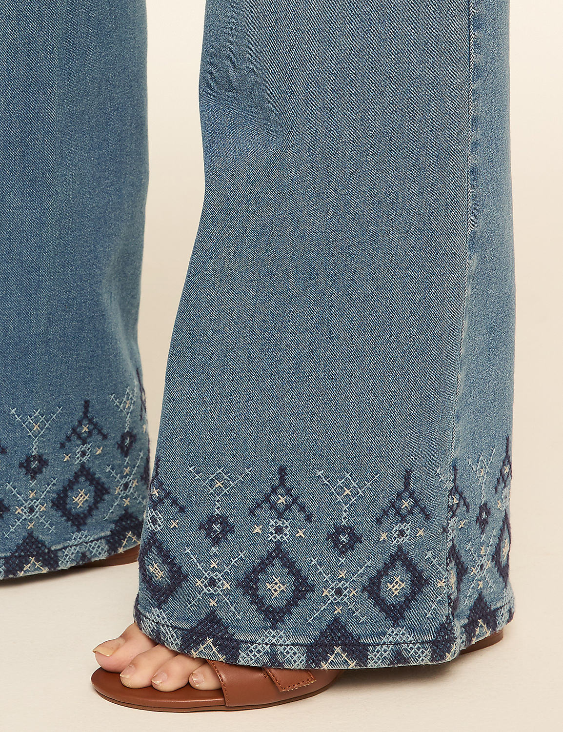 Faded blue denim bell-bottom jeans with embroidered geometric patterns at the hem are worn with brown sandals against a plain, light-colored background. Product Image 4