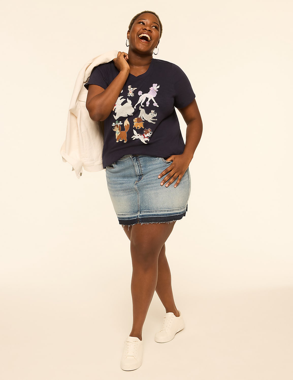 A woman in a graphic t-shirt and denim skirt smiles with a jacket over her shoulder against a plain, light-colored background. Product Image 3