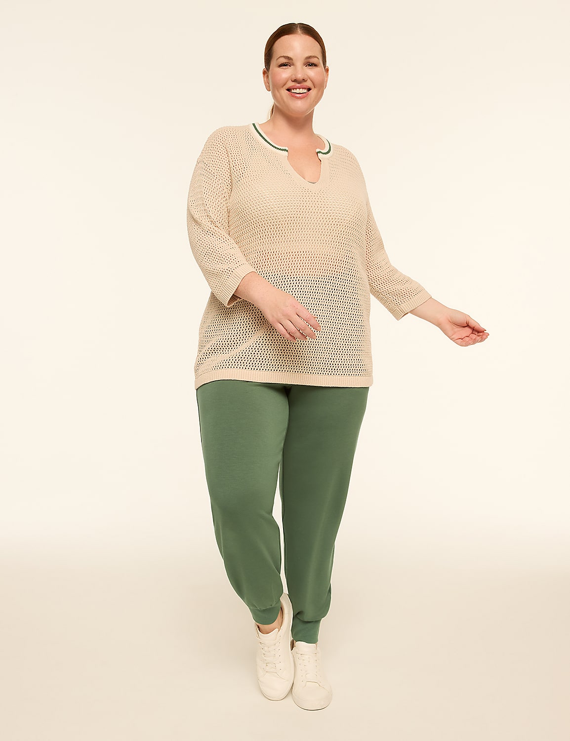 A smiling woman in a beige, open-knit top and green sweatpants stands against a plain, light background. Product Image 3