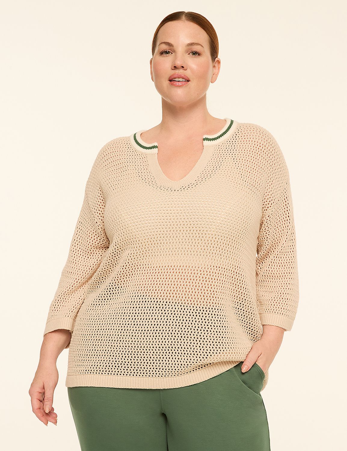 A woman in a beige, open-knit sweater with green trim stands against a plain, light-colored background. Product Image 1
