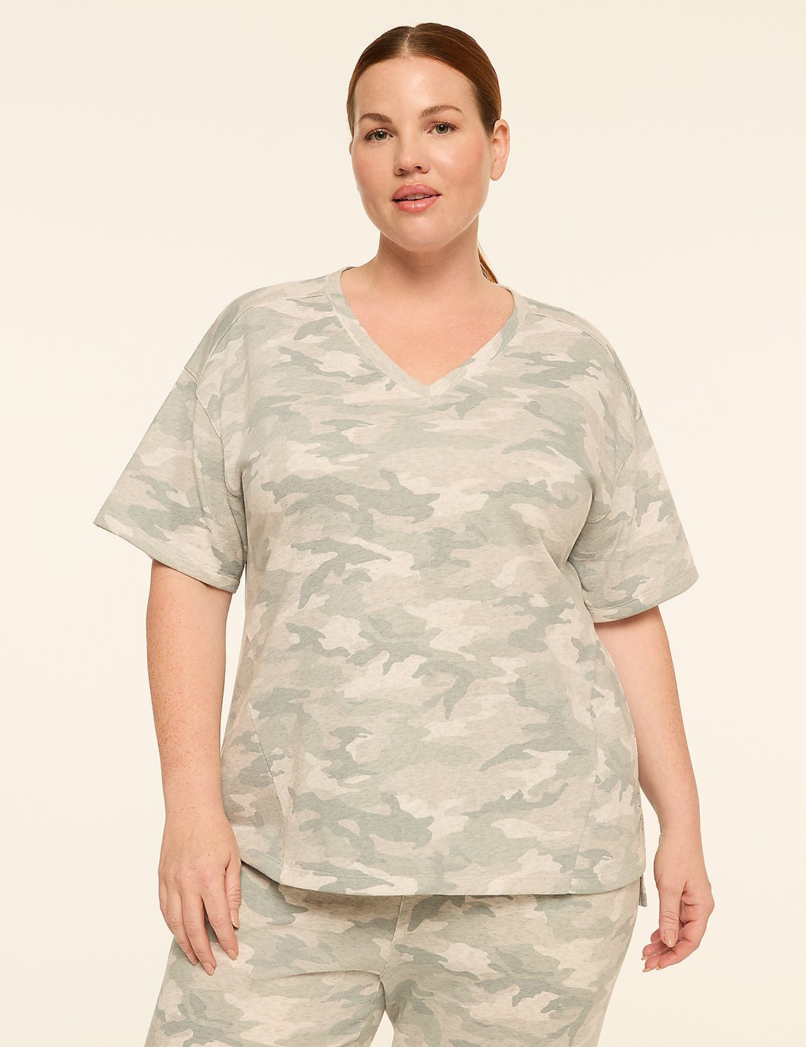 A woman in a light green camouflage v-neck t-shirt and matching pants stands against a plain, light beige background. Product Image 1