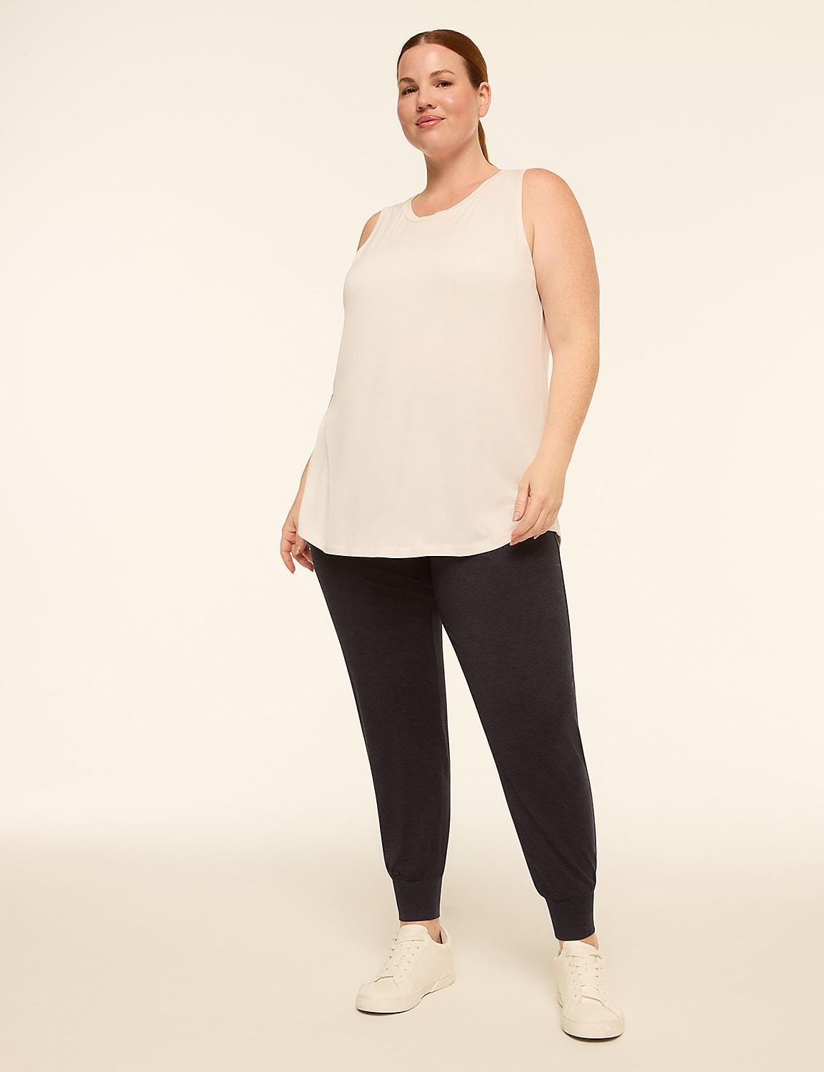 A woman in a light pink tank top and dark blue joggers stands against a plain, light background. Product Image 3