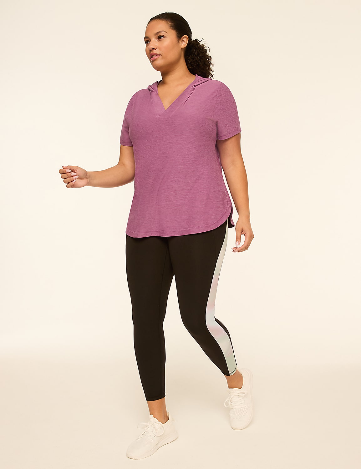 A woman in a purple hooded shirt and black leggings with white stripes walks against a plain, light-colored background. Product Image 3