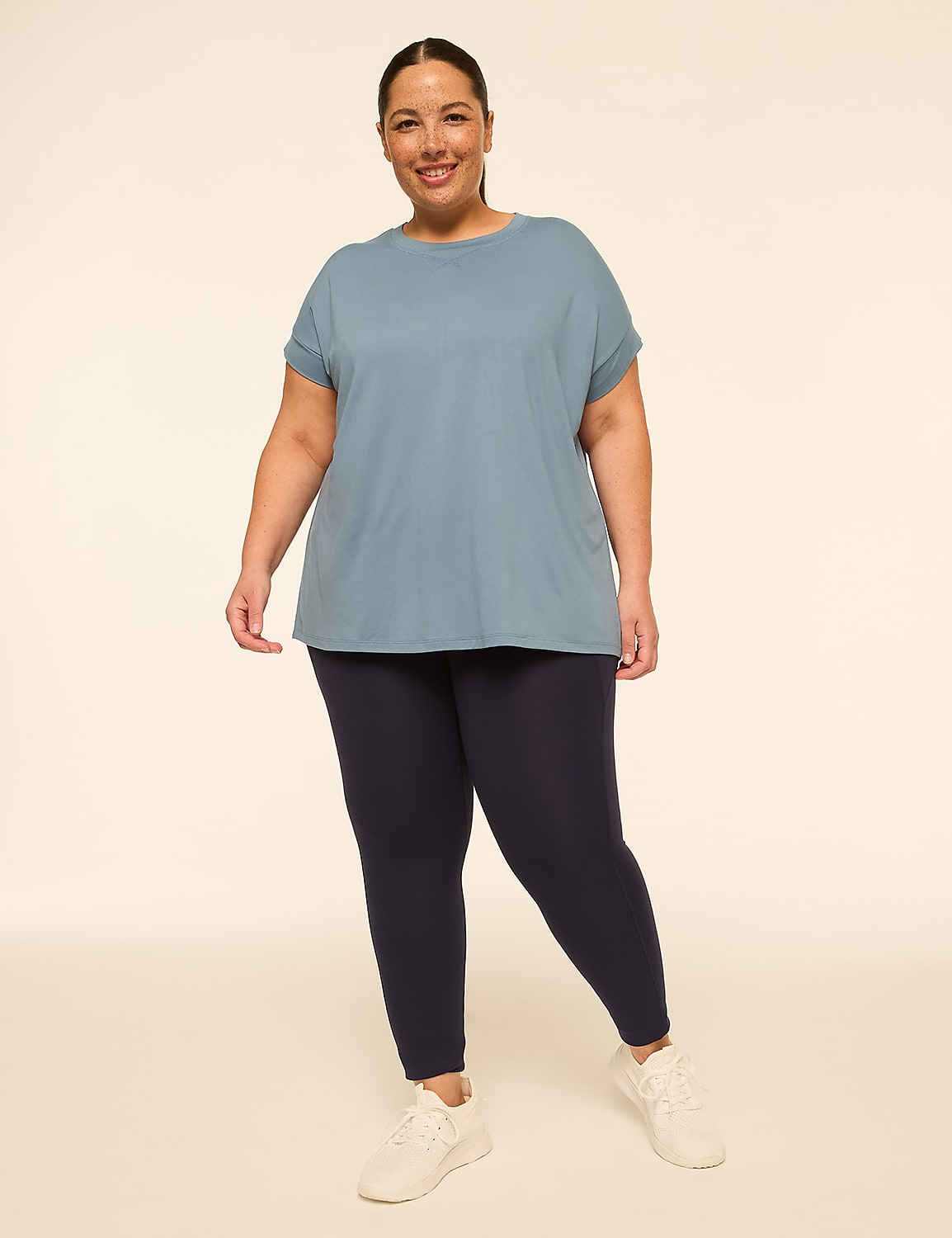A smiling woman in a blue t-shirt and navy leggings stands against a plain, light-colored background. Product Image 3