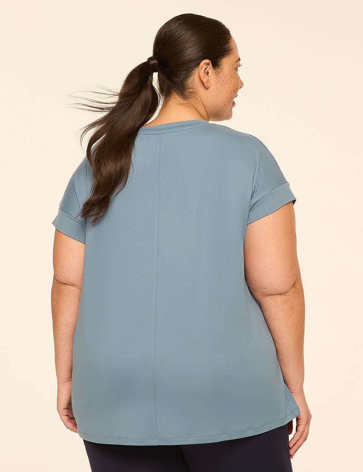 A woman with dark hair pulled into a ponytail stands facing away from the camera, wearing a blue t-shirt and dark pants, against a plain, light-colored background. Product Image 2