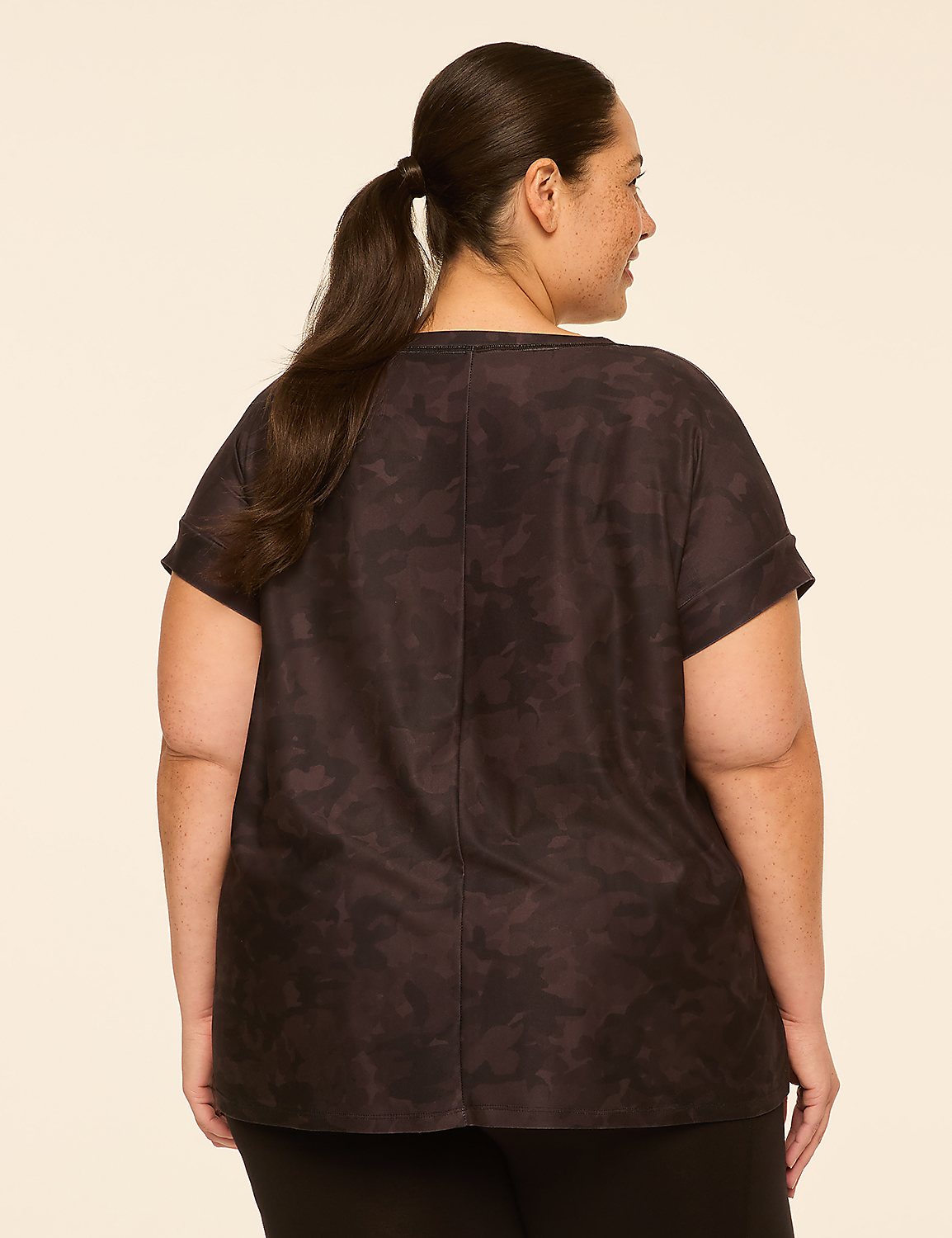 A woman with dark hair in a ponytail, wearing a dark patterned t-shirt, stands against a plain, light-colored background. Product Image 2