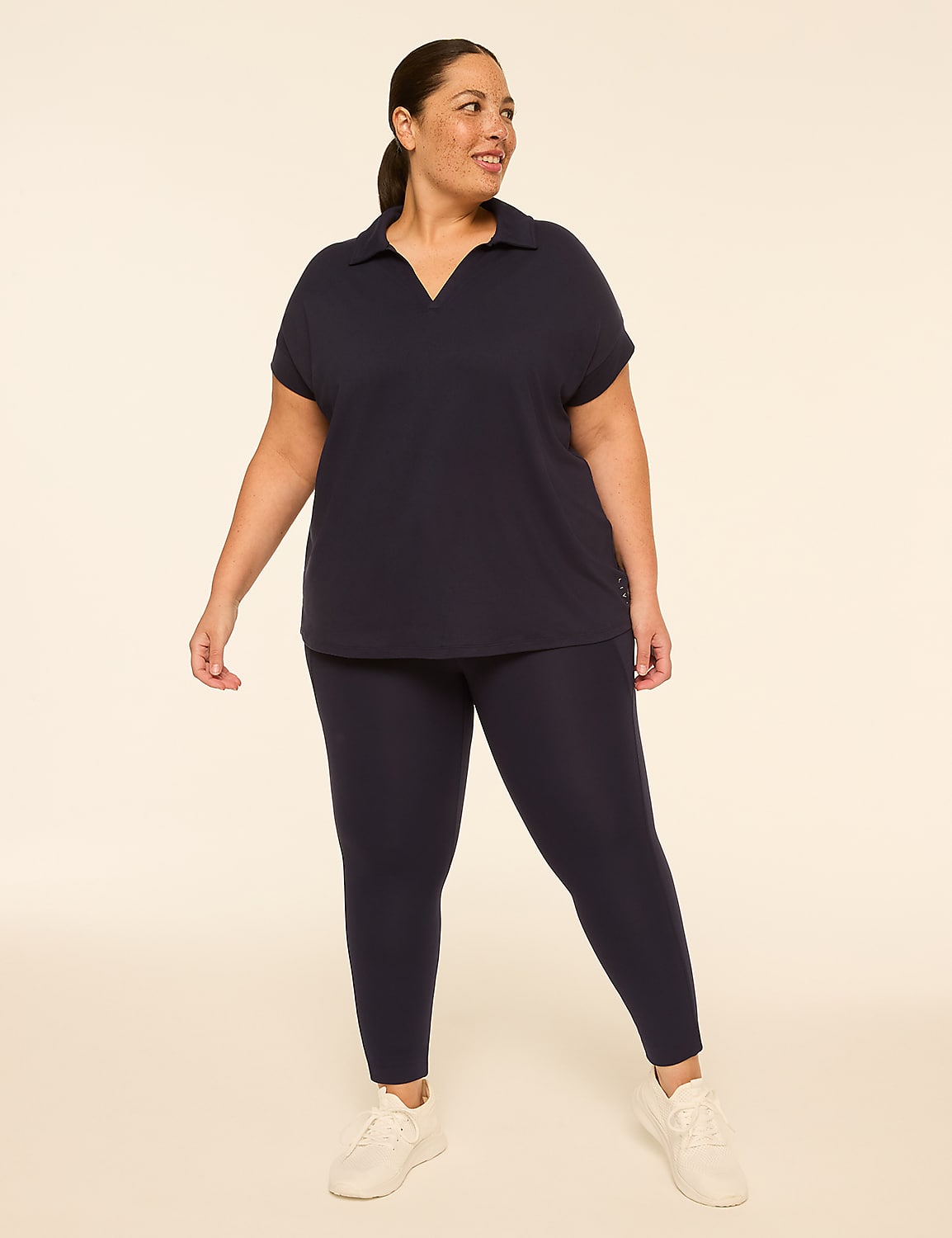 A woman in a navy blue polo shirt and leggings stands against a plain, light-colored background. Product Image 3