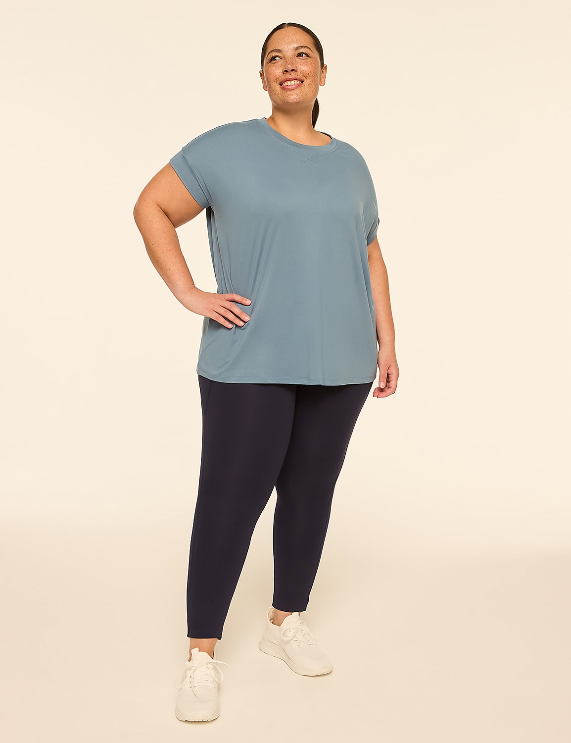 A woman in a blue t-shirt and navy leggings stands with her hand on her hip against a plain, light-colored background. Product Image 3