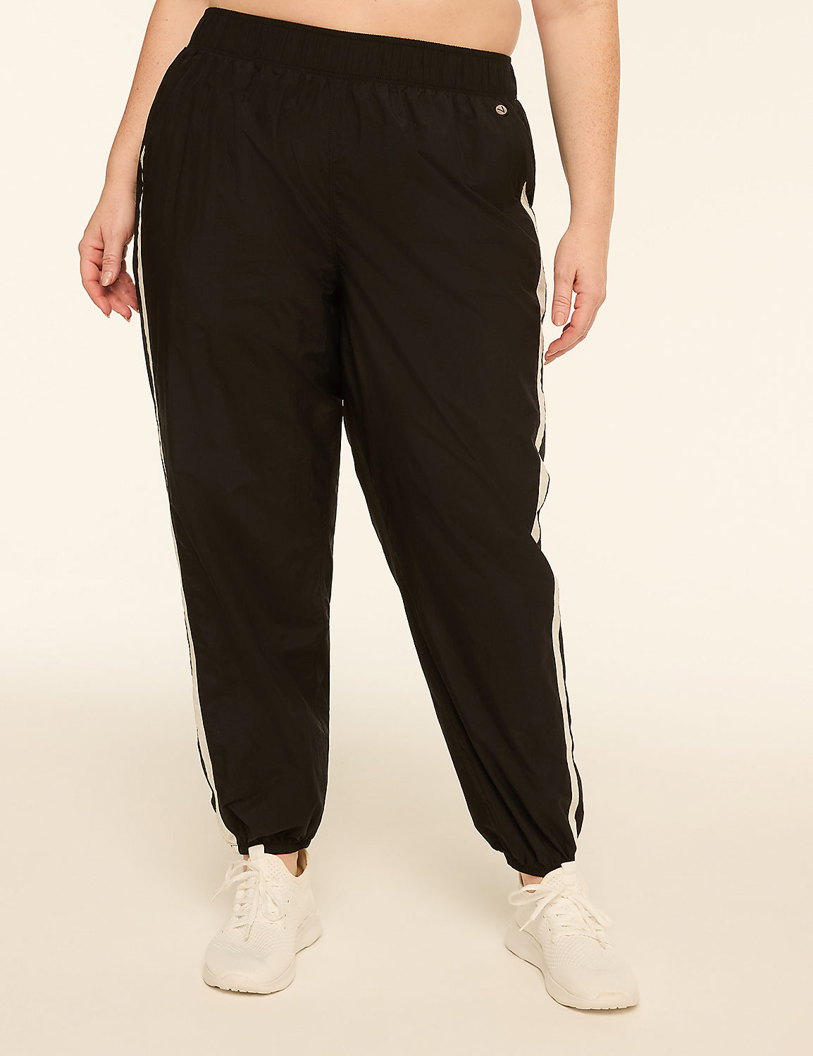 A person stands in black track pants with white stripes and white sneakers against a plain, light-colored background. Product Image 3