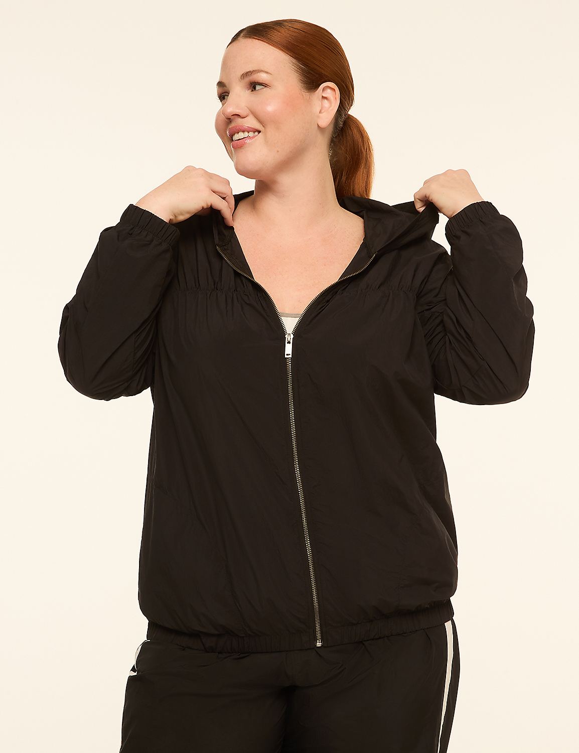 A smiling woman in a black hooded jacket stands against a plain, light-colored background. Product Image 1