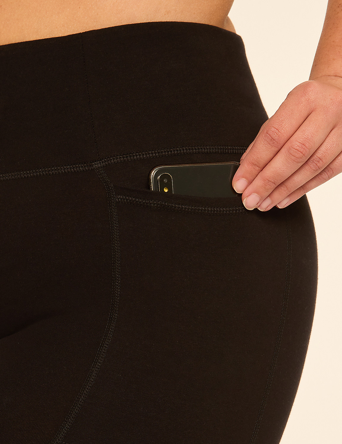 A hand places a smartphone into the pocket of black leggings against a plain background. Product Image 4
