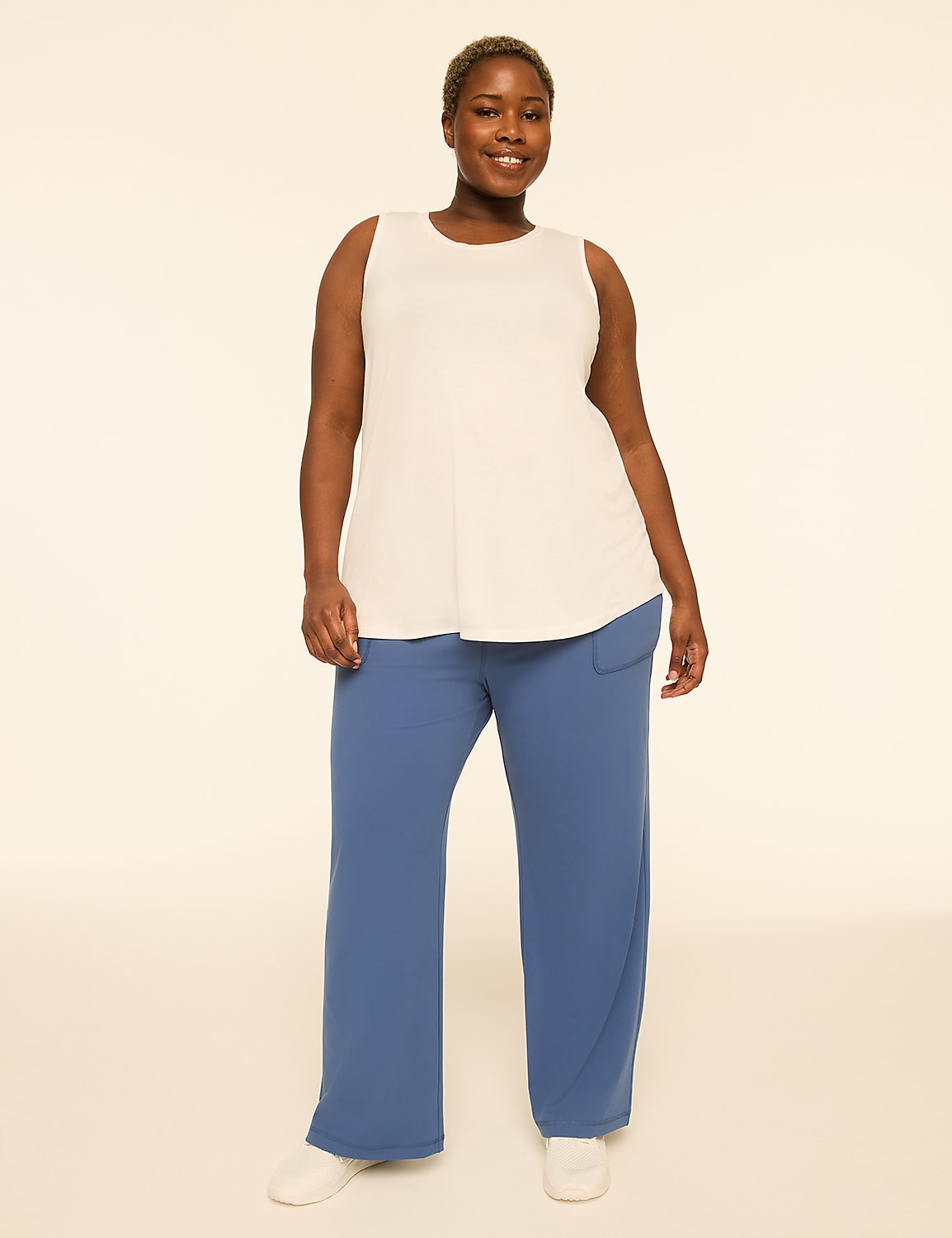 A smiling woman in a white tank top and blue pants stands against a plain, light background. Product Image 3