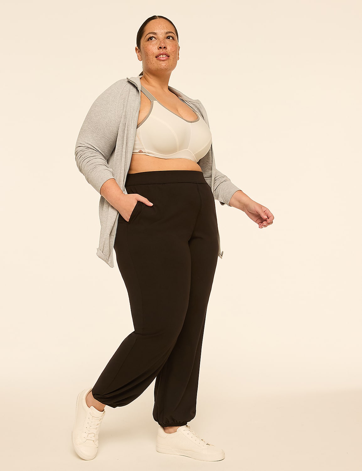 A woman in black sweatpants, a sports bra, and a grey hoodie stands against a plain, light-colored background. Product Image 3