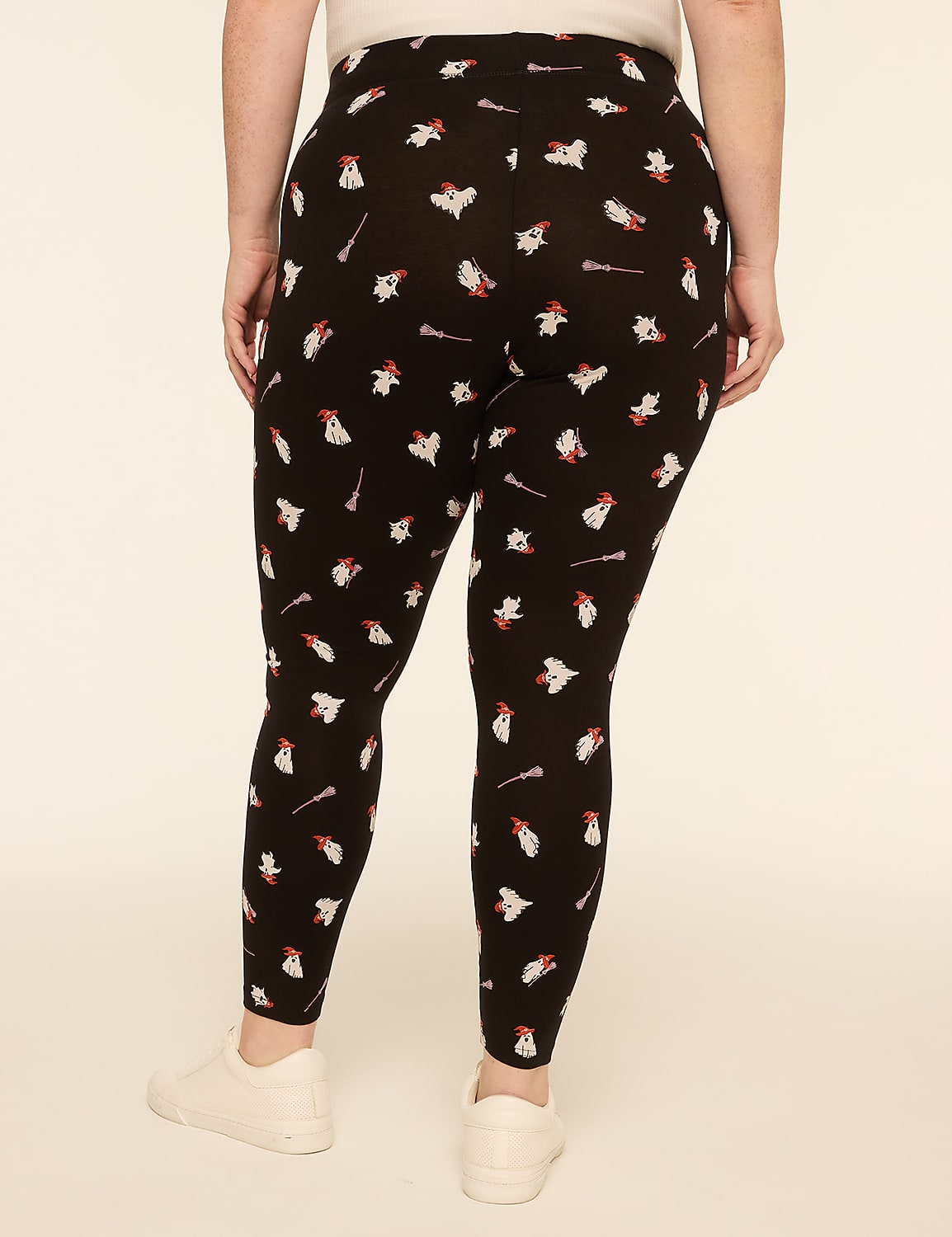 A person wearing black leggings with a repeating pattern of white ghosts and red candy canes stands against a plain, light beige background. Product Image 2
