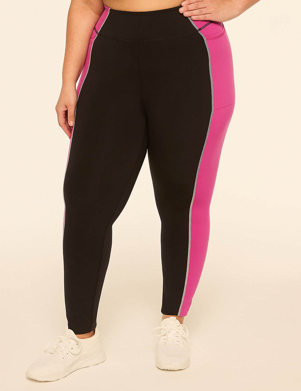 A person wearing black leggings with pink side panels and white sneakers stands against a plain, light-colored background. Product Image 1