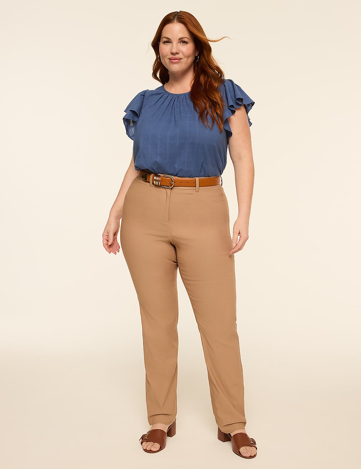 A woman with auburn hair stands in a studio setting, wearing a blue ruffled-sleeve blouse and tan pants against a plain cream background. Product Image 3