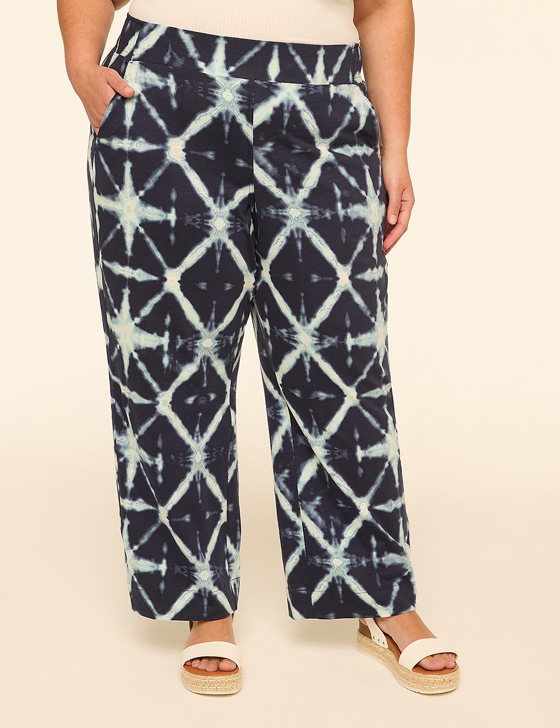 A person stands in the foreground wearing dark blue and white tie-dye pants and sandals, against a plain, light tan background. Product Image 1