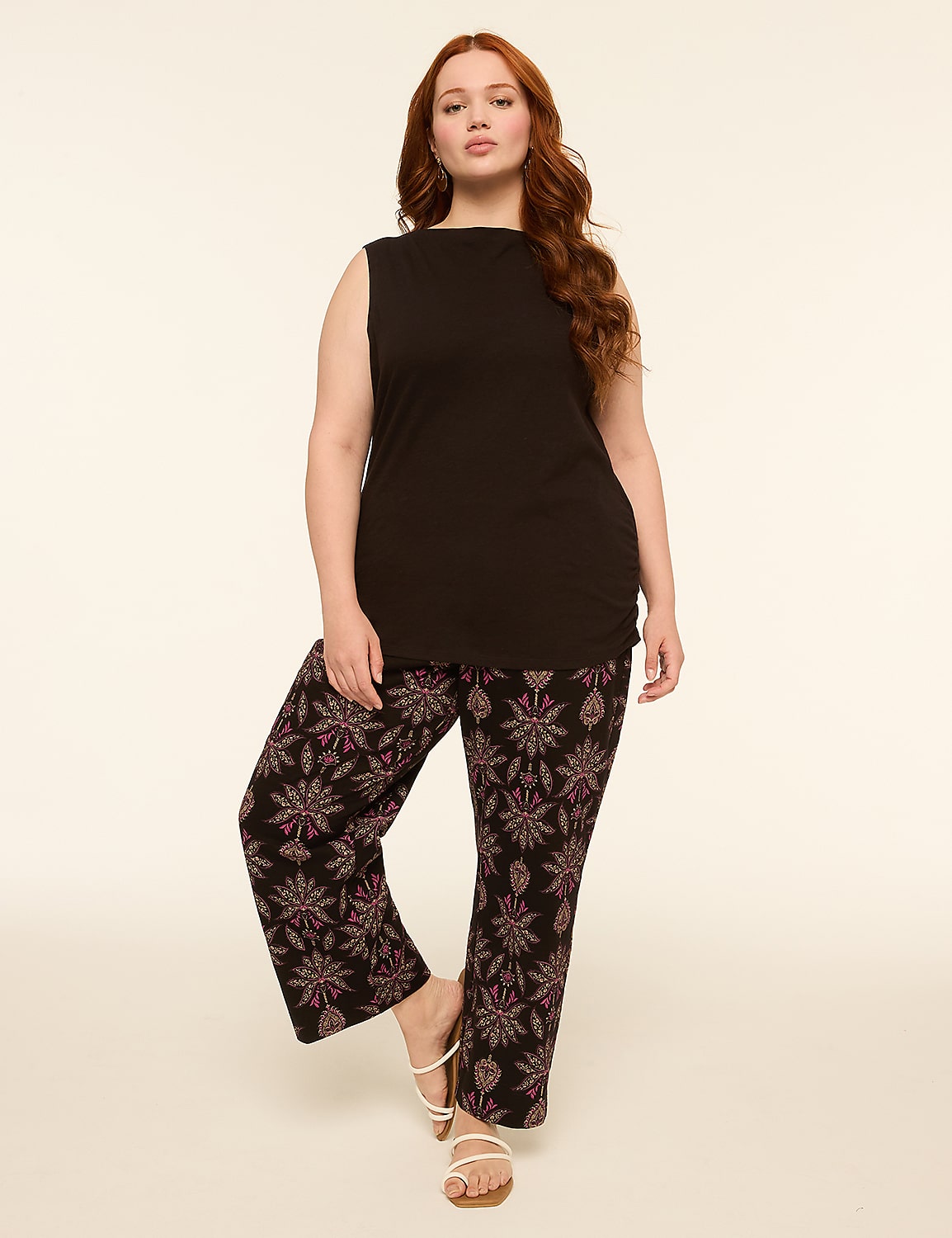 A woman with red hair stands in a black sleeveless top and patterned pants against a plain, light-colored background. Product Image 3