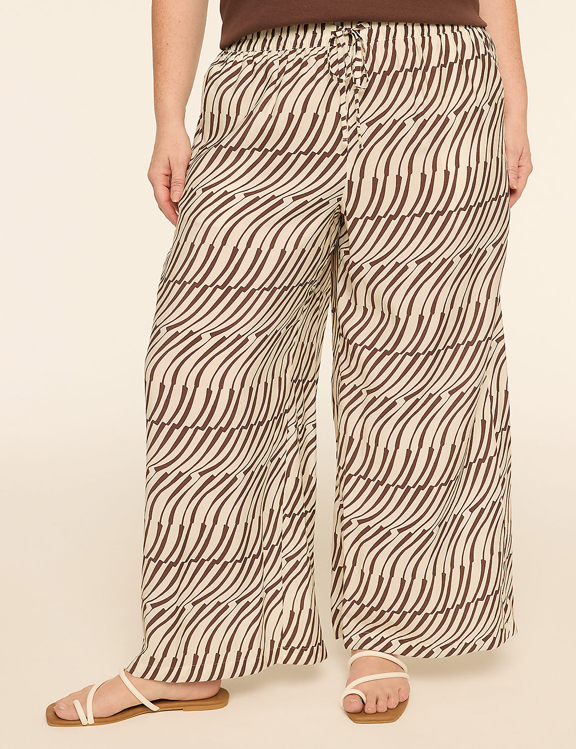 A person stands wearing wide-leg pants with a brown and cream wavy pattern, against a plain, light-colored background. Product Image 1