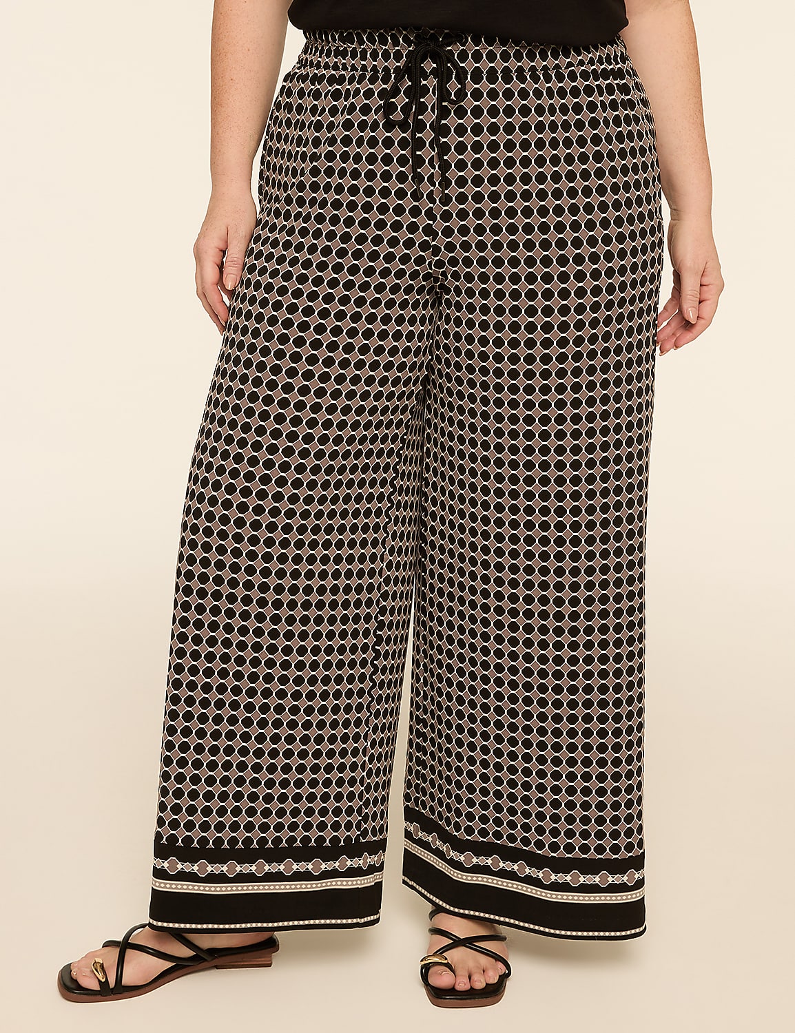 A person stands in wide-leg patterned pants with a geometric design and a plain background. Product Image 1