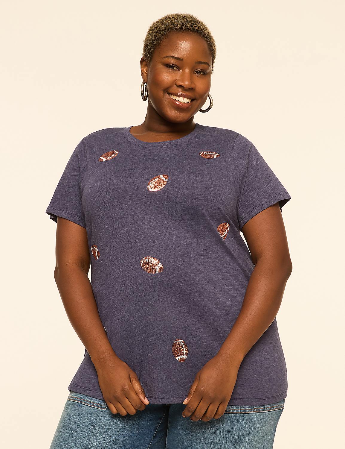 A smiling woman with short hair wears a navy blue t-shirt with football graphics, standing against a plain cream background. Product Image 1